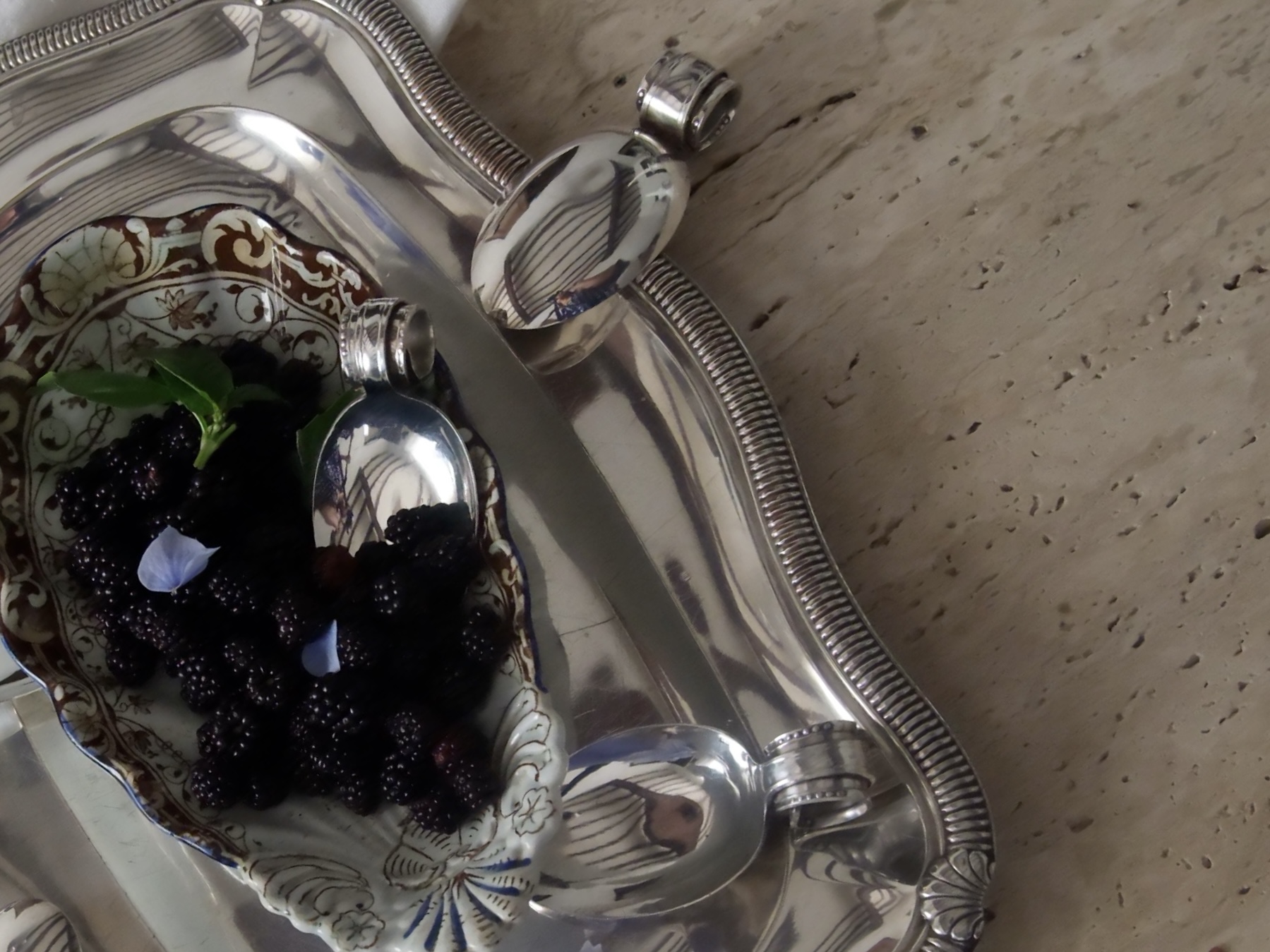 Tasting spoons styled on a silver tray beside a bowl of seasonal blackberries
