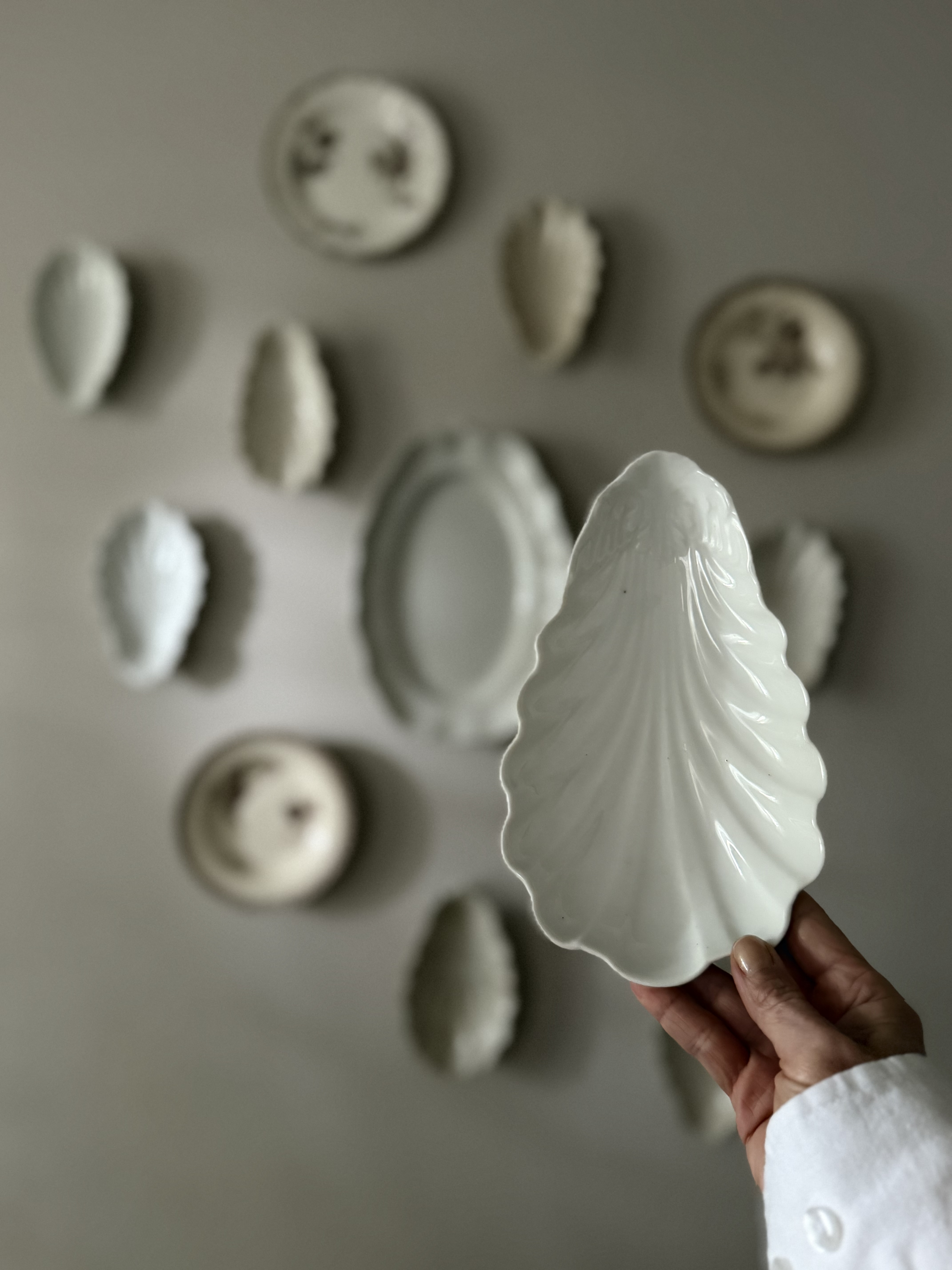 Hand holding the white faïence ravier against a backdrop of antique plates