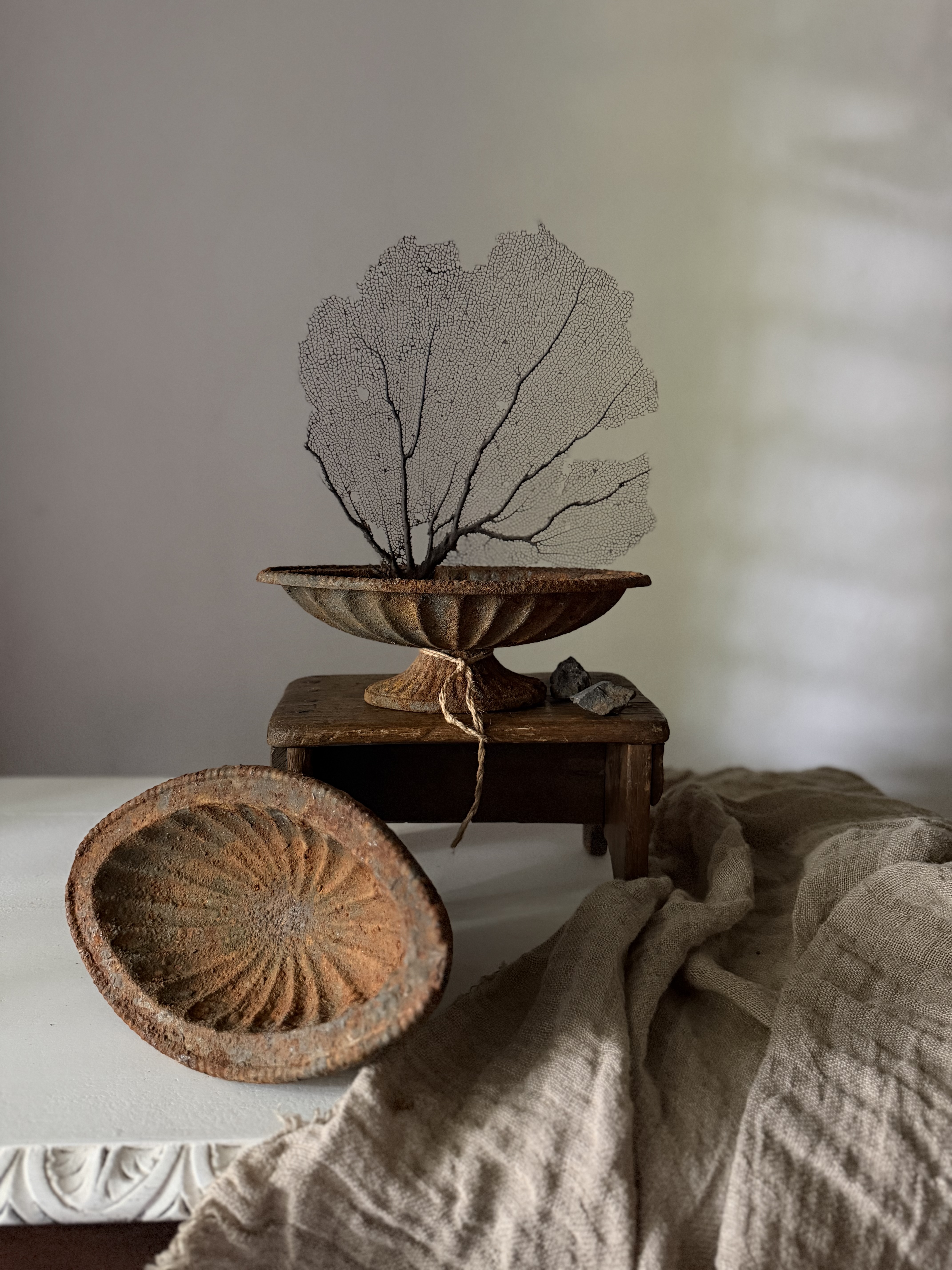 Two rusted cast iron jardinieres staggered on and beside an antique wooden stool